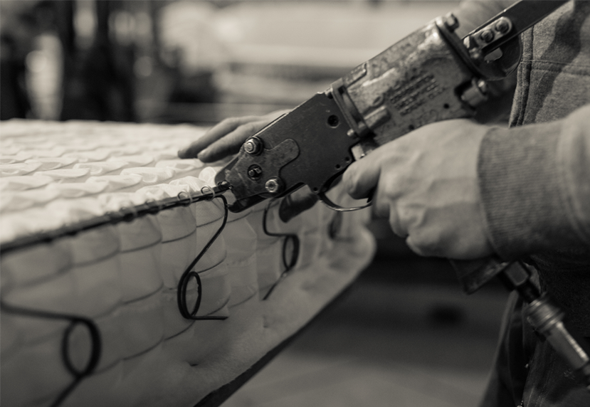 Worker assembling mattress springs with a precision fastening tool.