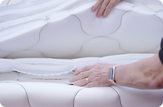 Hands pressing layered mattress foam to demonstrate comfort and support